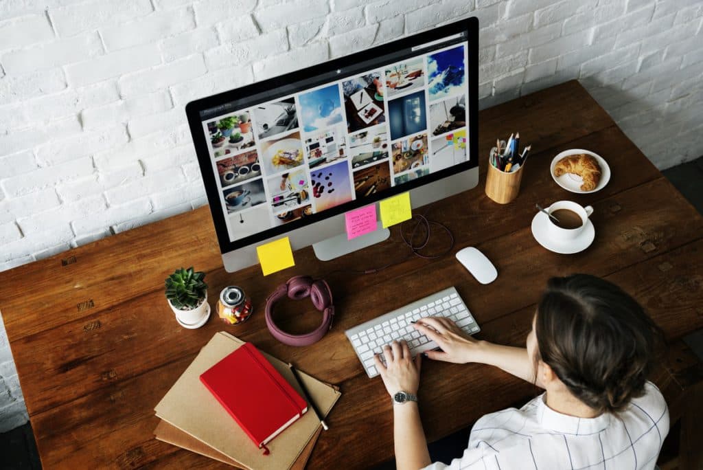 A woman types at her desktop computer while viewing colorful images on the screen.
