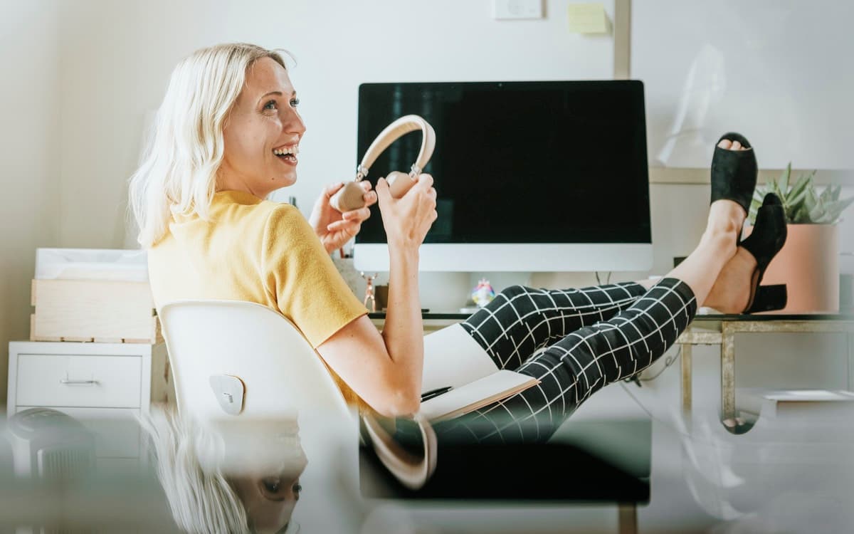 A woman prepares to put on her wireless headphones as she relaxes at her desk before a video conference.