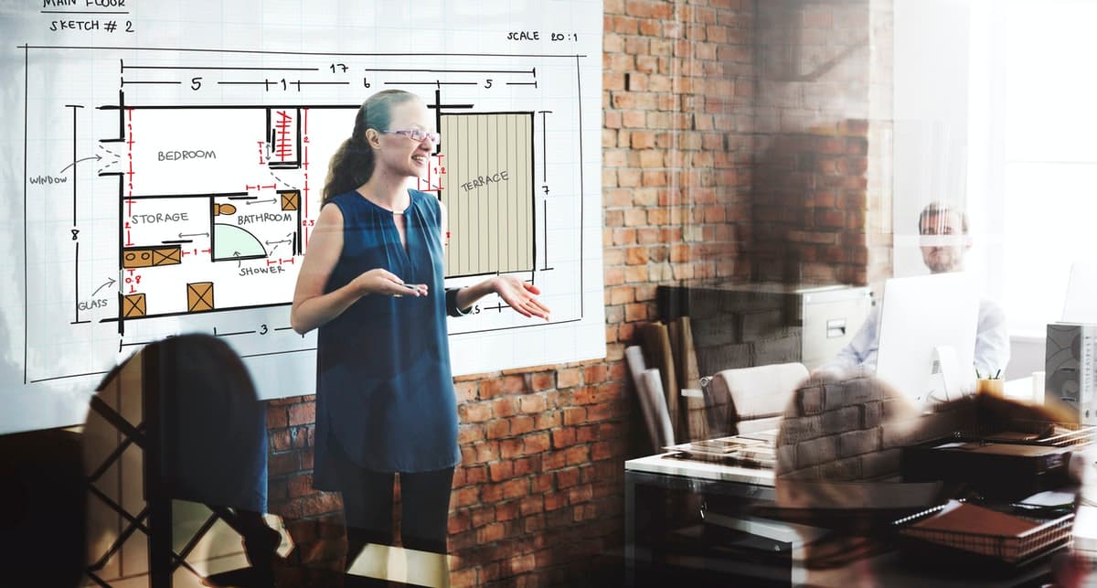 A woman leads her team through floor plan designs during a brainstorming session.