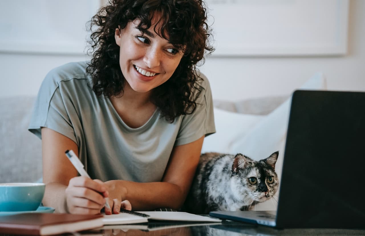 A woman takes notes while watching a webinar on her laptop.