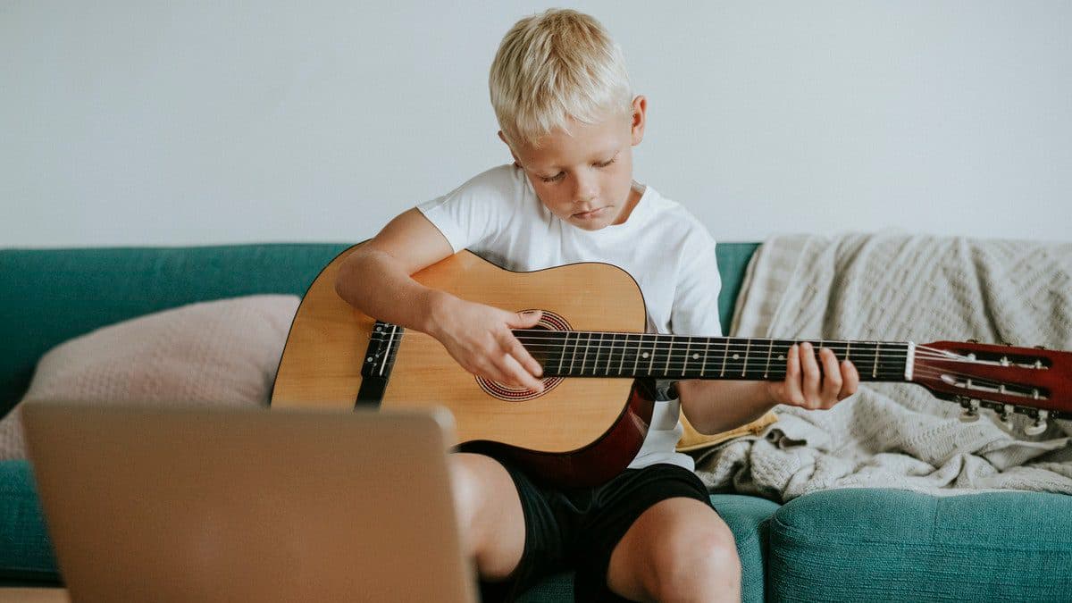 A child takes part in an online guitar class while sitting on the couch at home.