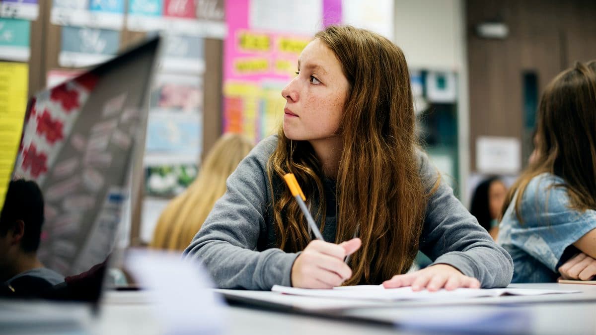 A student looks at the interactive whiteboard while taking notes during class.