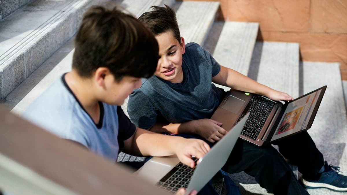 Two students complete classwork using hybrid learning tools on their school laptops.