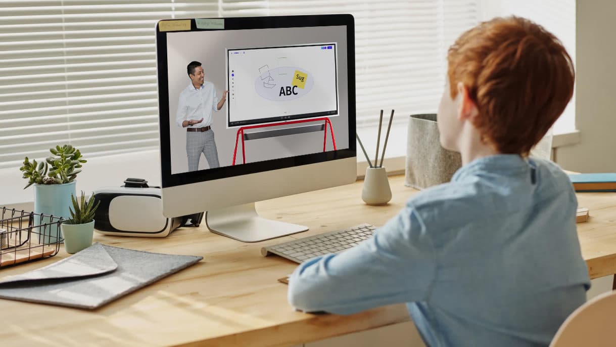 A student takes part in a distance learning class from home while his teacher utilizes interactive whiteboarding.